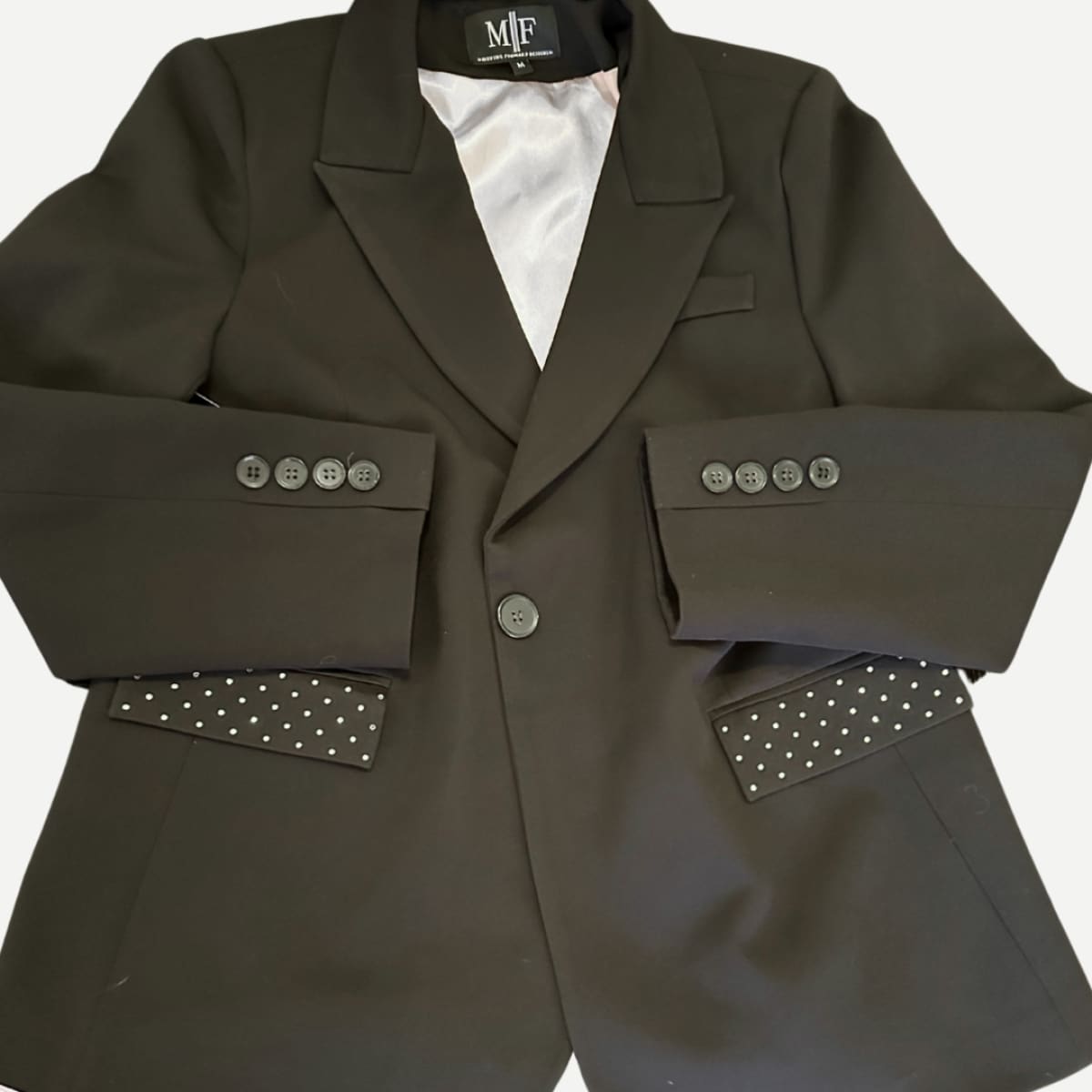 Dark gray blazer with decorative buttons and studded details on a white background