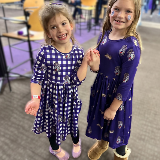 Two young girls in matching blue dresses with logos, holding hands indoors.