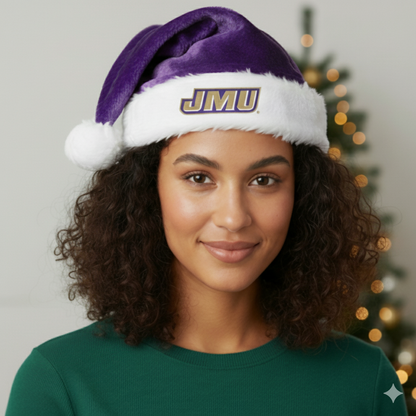 Person wearing a purple and white Santa hat with 'JMU' on it, standing in front of a Christmas tree.