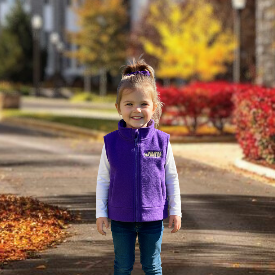 Young girl wearing a purple vest with a logo, standing outdoors in autumn.