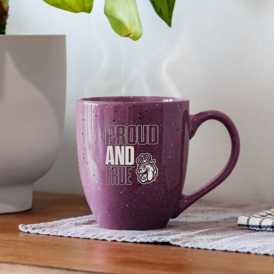 Purple mug with 'Proud and True' text on a wooden surface with a plant in the background