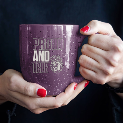 Purple mug with 'Proud and True' text held by hands with red nail polish against a dark background