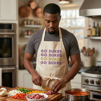 Man in a kitchen wearing a 'Go Dukes' apron, preparing food.