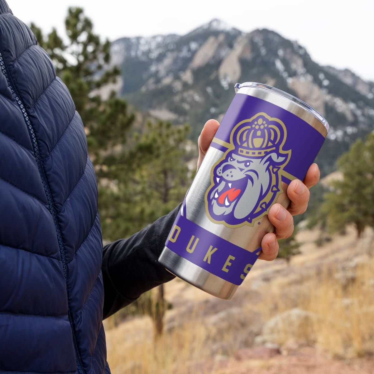 Person holding a purple tumbler with a logo against a mountainous background