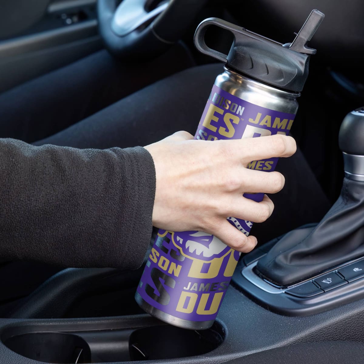 Person holding a purple and silver water bottle with text in a car.