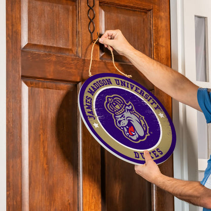 Person hanging a James Madison University door sign on a wooden door.