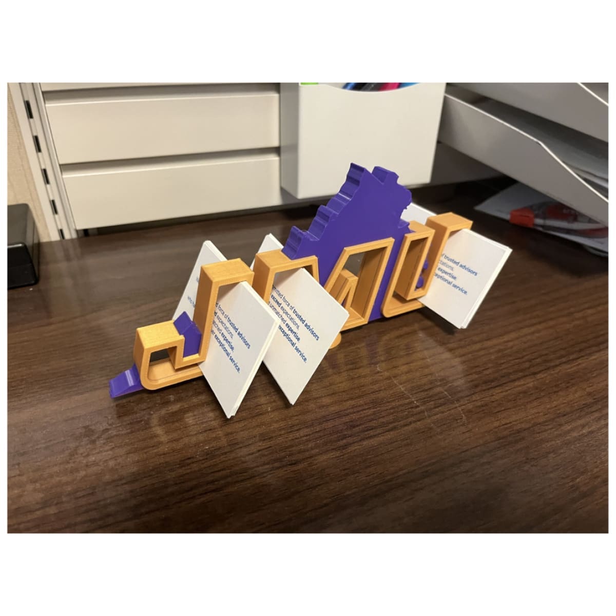 View of the JMU Desk Decor showing the thickness and structure of the gold letters and purple background. HOLDING BUSINESS CARDS