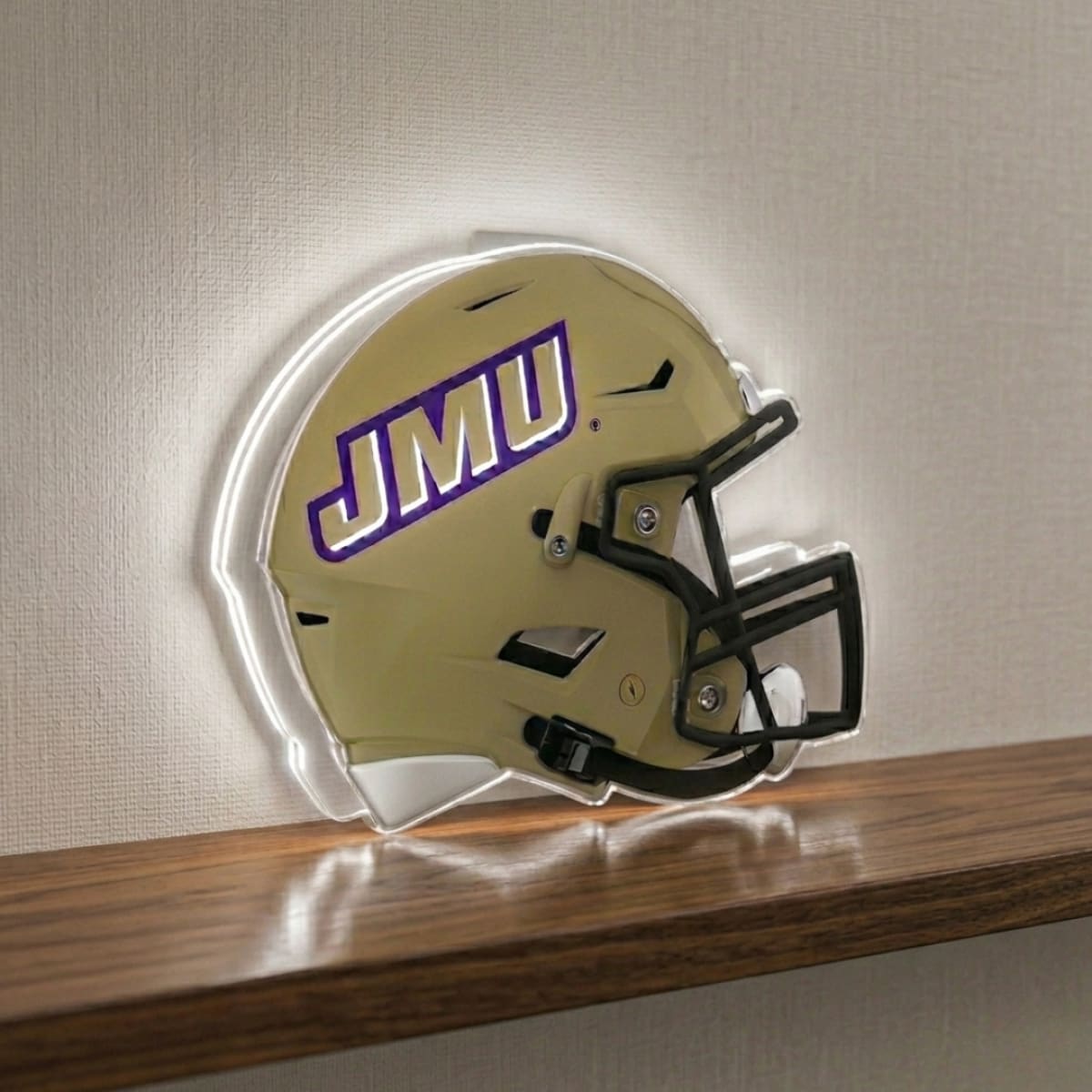Gold football helmet with 'JMU' logo on a wooden shelf against a beige wall