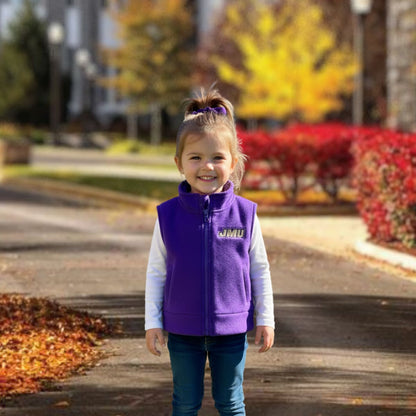Young girl wearing a purple vest with a logo, standing outdoors in autumn.